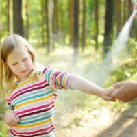 Mother applying insect repellent to her daughter before forest hike on a summer day.