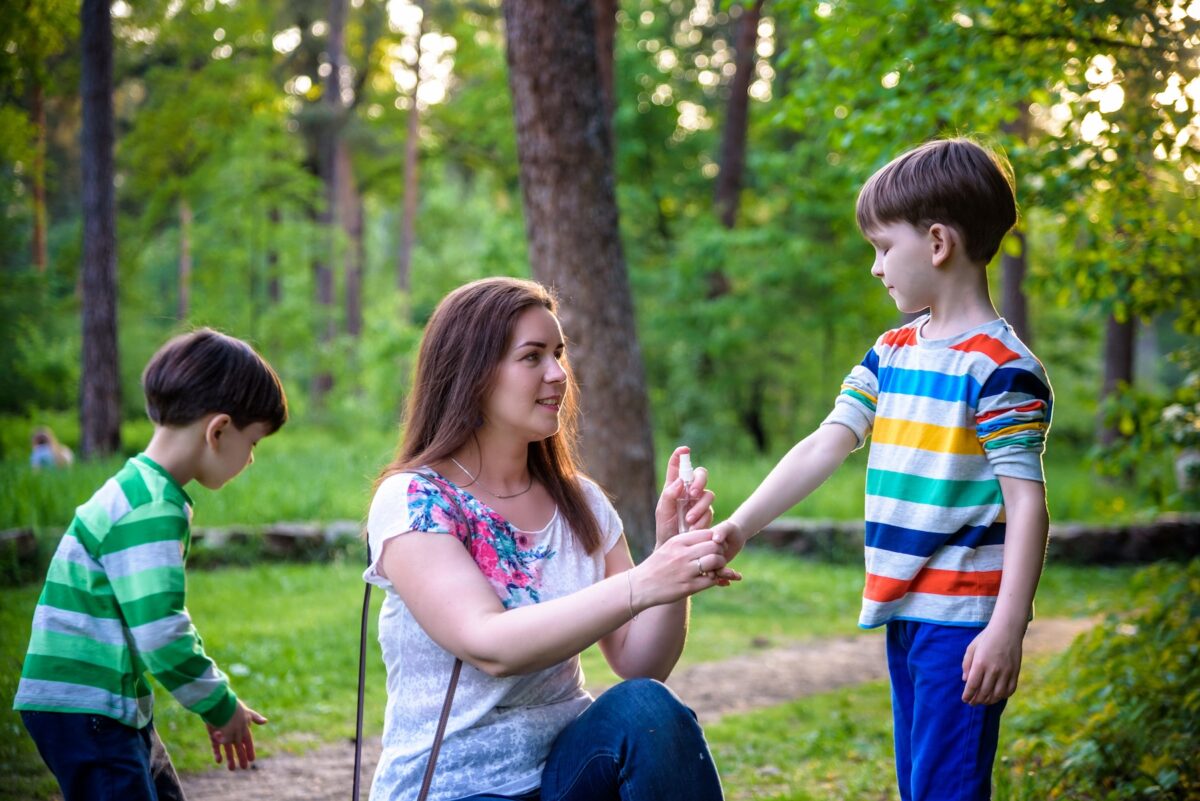Young mother applying bug spray to her two sons before summer hike.