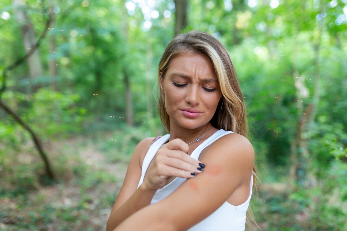 Young woman scratching bug bite on upper arm while out for a hike.