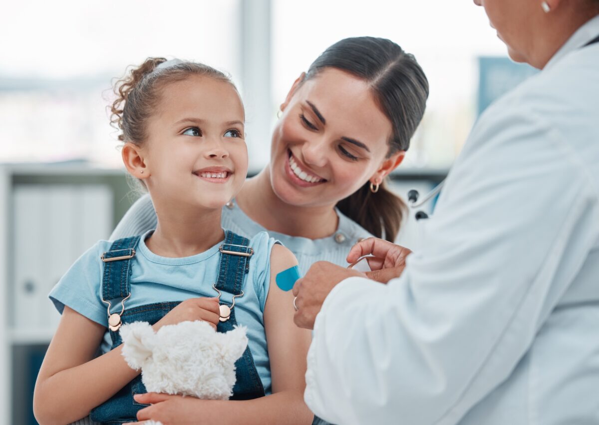Mom holding daughter as a doctor gives her a flu vaccine injection
